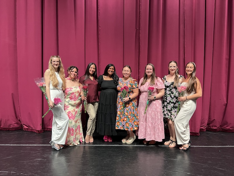 Dance teachers dressed up and posing for photo, with flowers.